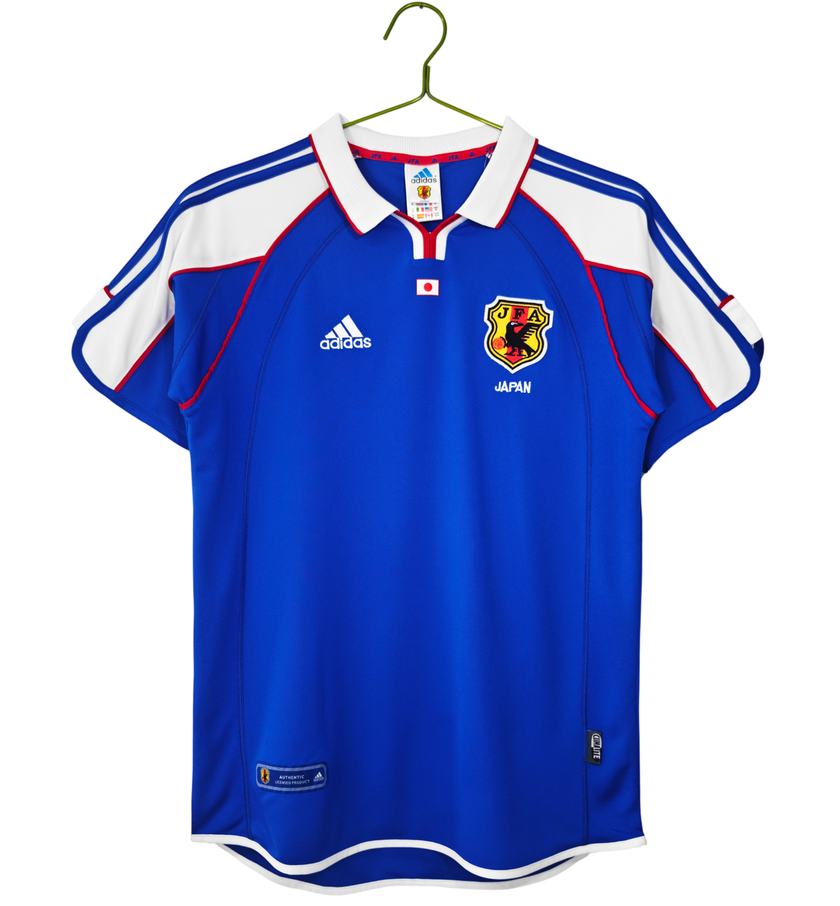 A blue and white short-sleeve soccer jersey with red trim, featuring the Adidas logo and the Japan national team crest, hanging on a green hanger against a white background.