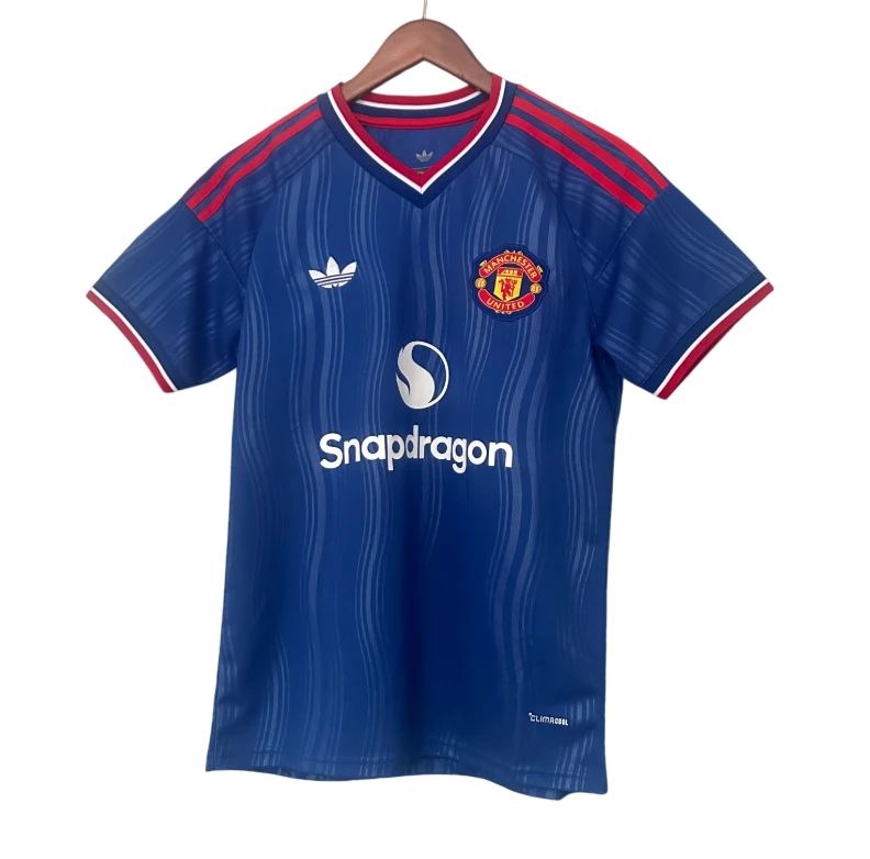 A blue Manchester United soccer jersey by Adidas, featuring red and white trim, the club crest, and the Snapdragon sponsor logo, displayed on a wooden hanger against a white background.