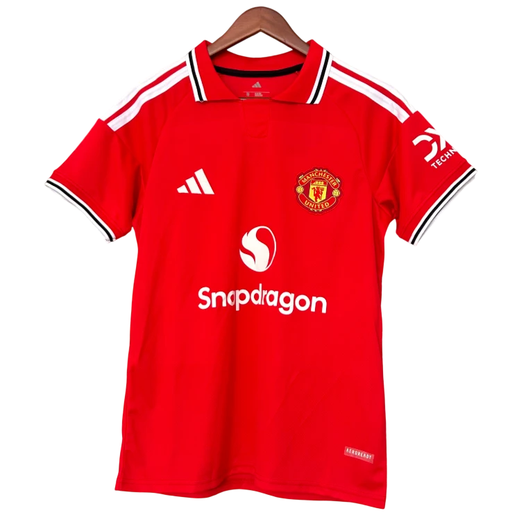 A red Manchester United short-sleeve soccer jersey by Adidas, featuring the club crest, white 'Snapdragon' sponsor logo, and a wooden hanger against a plain white background.