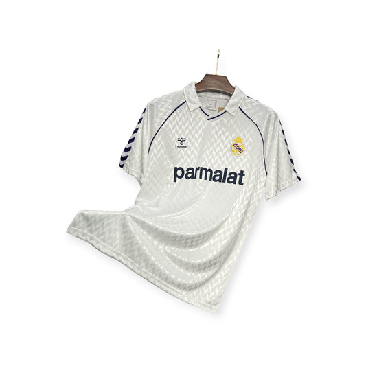 Real Madrid 1988/1989 Home Jersey displayed on a hanger, predominantly white with blue and yellow details, and the 'pamalat' brand logo.